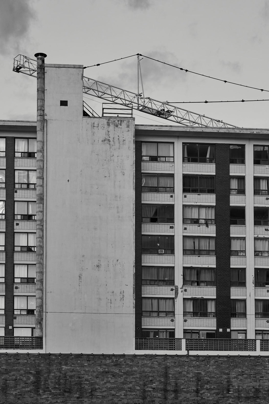 Crane extends over apartment building under cloudy sky.
